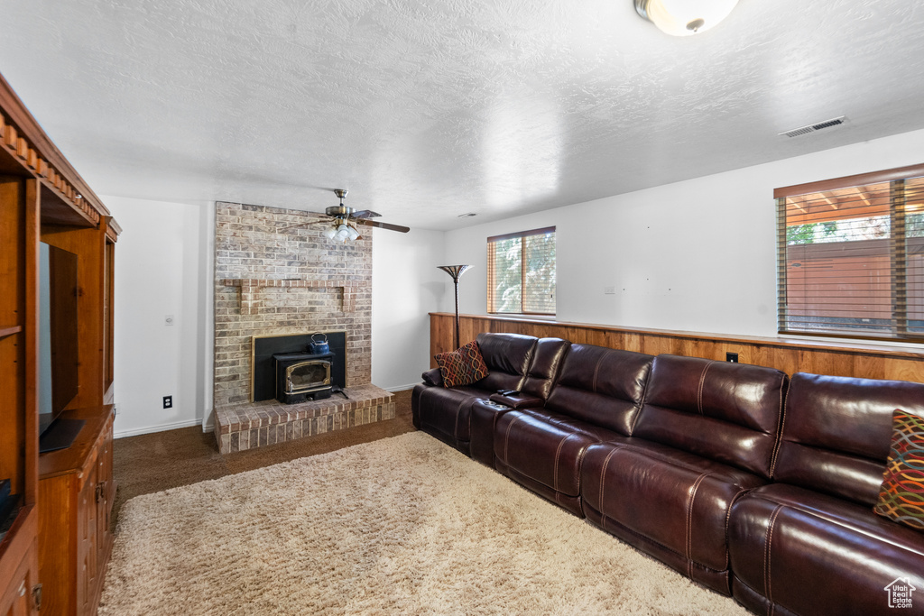 Carpeted living area with a wood stove, plenty of natural light, a ceiling fan, and a textured ceiling