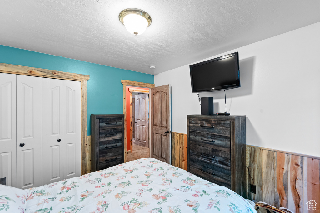 Bedroom featuring wainscoting, wood walls, a closet, and a textured ceiling