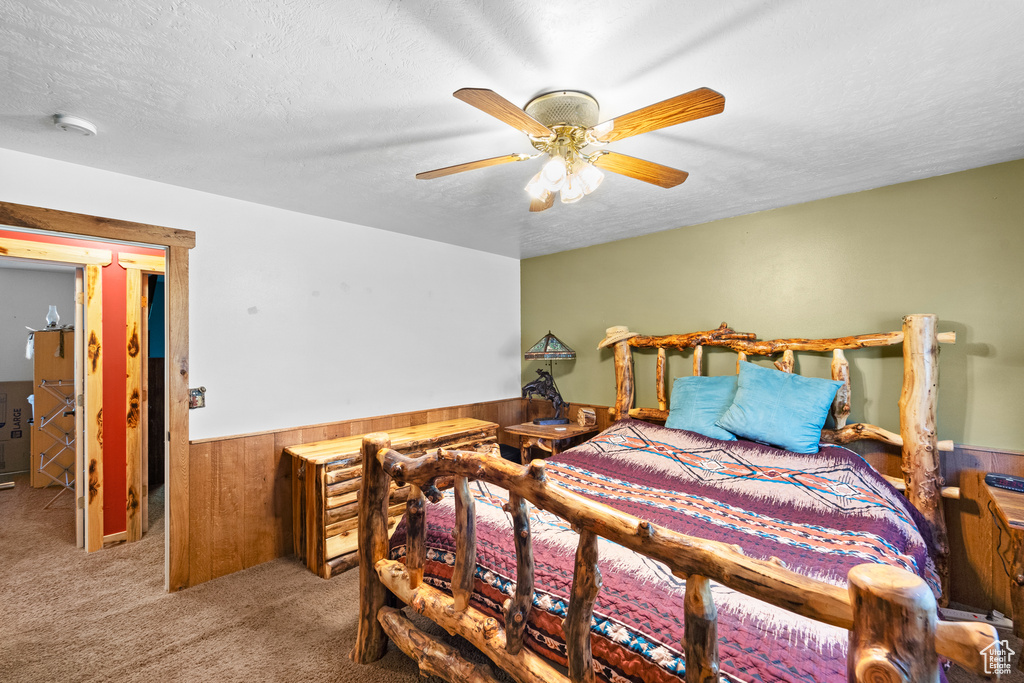Bedroom with wood walls, a wainscoted wall, carpet, a textured ceiling, and a ceiling fan