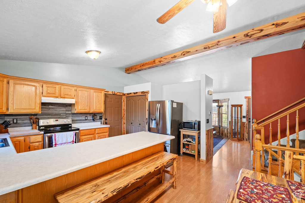 Kitchen featuring stainless steel appliances, under cabinet range hood, light countertops, decorative backsplash, and light wood-style flooring