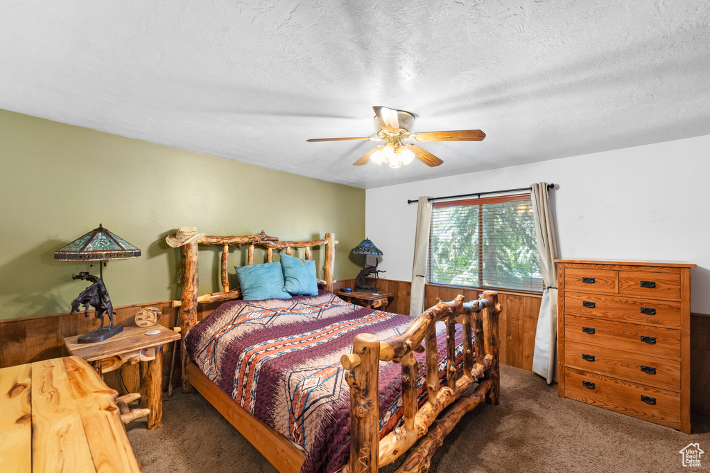 Carpeted bedroom featuring wood walls, ceiling fan, a wainscoted wall, and a textured ceiling