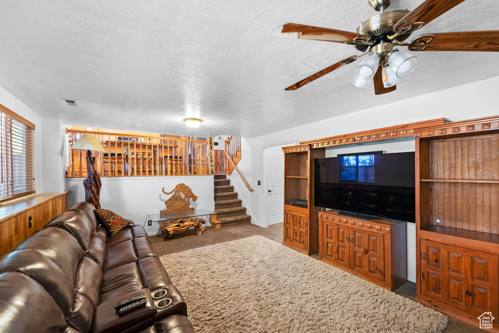 Living area with stairway, carpet floors, ceiling fan, and a textured ceiling