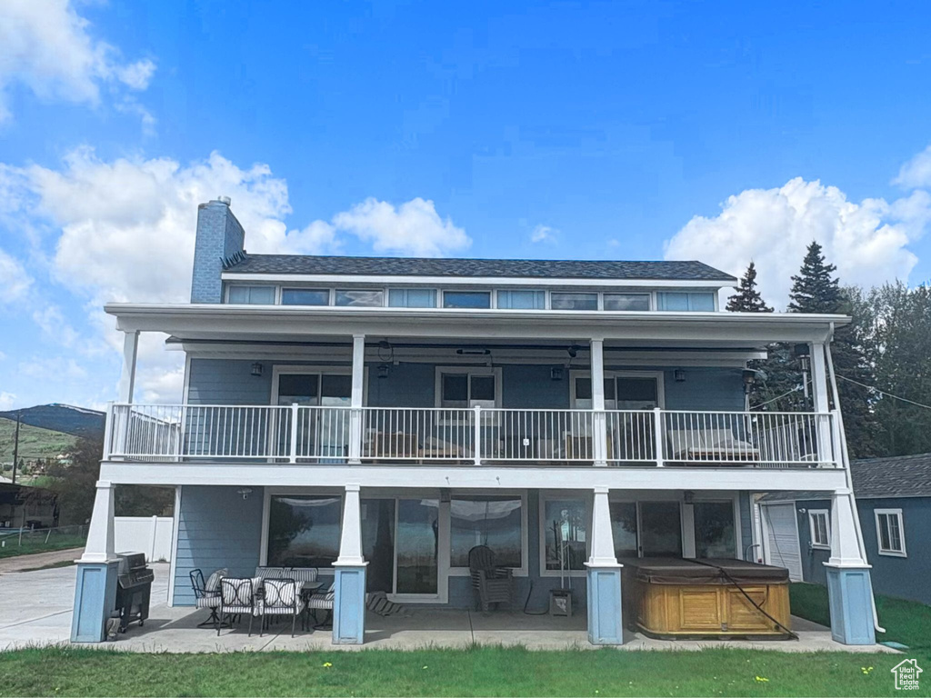 Back of house featuring a hot tub, a balcony, a patio area, and a chimney