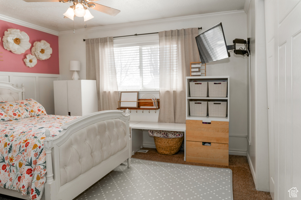 Carpeted bedroom with a wainscoted wall, crown molding, and a ceiling fan