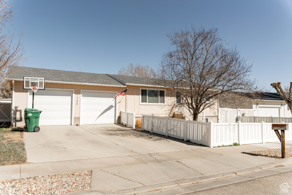 View of front of house with an attached garage, a fenced front yard, concrete driveway, and a shingled roof