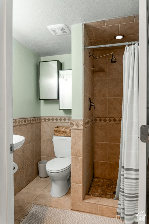 Full bath with tile patterned flooring, tile walls, toilet, visible vents, and tiled shower