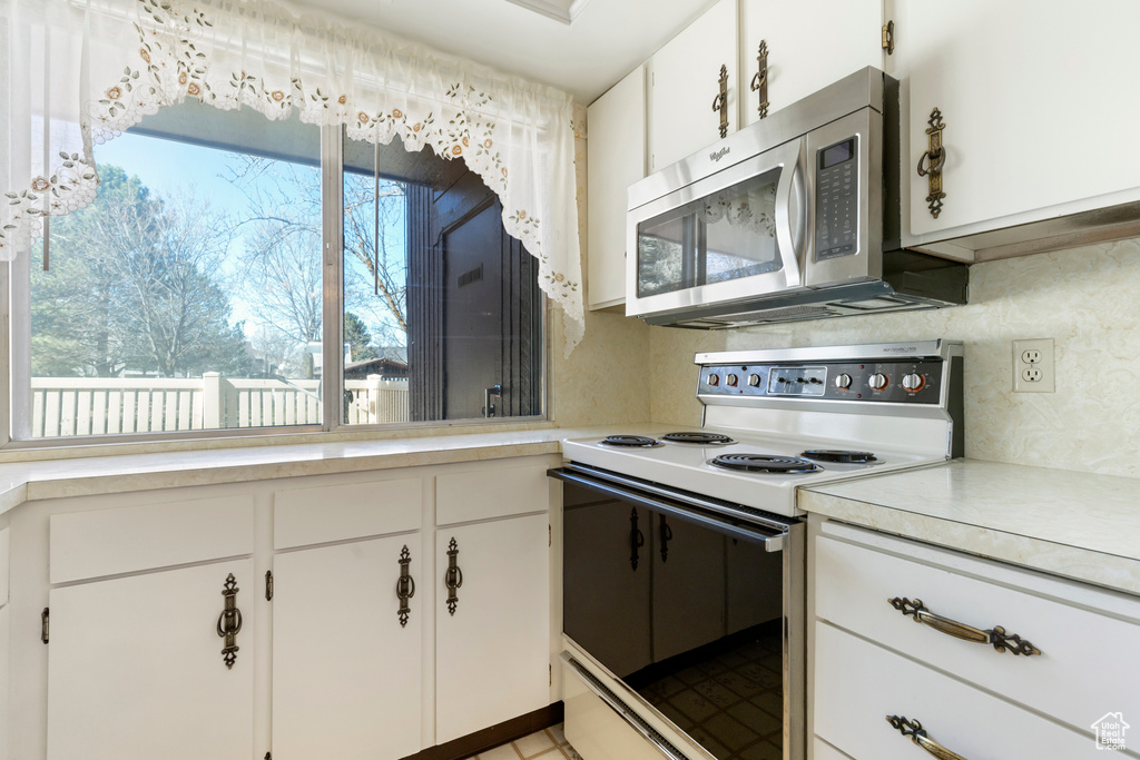 Kitchen with stainless steel microwave, light countertops, range with electric cooktop, and decorative backsplash