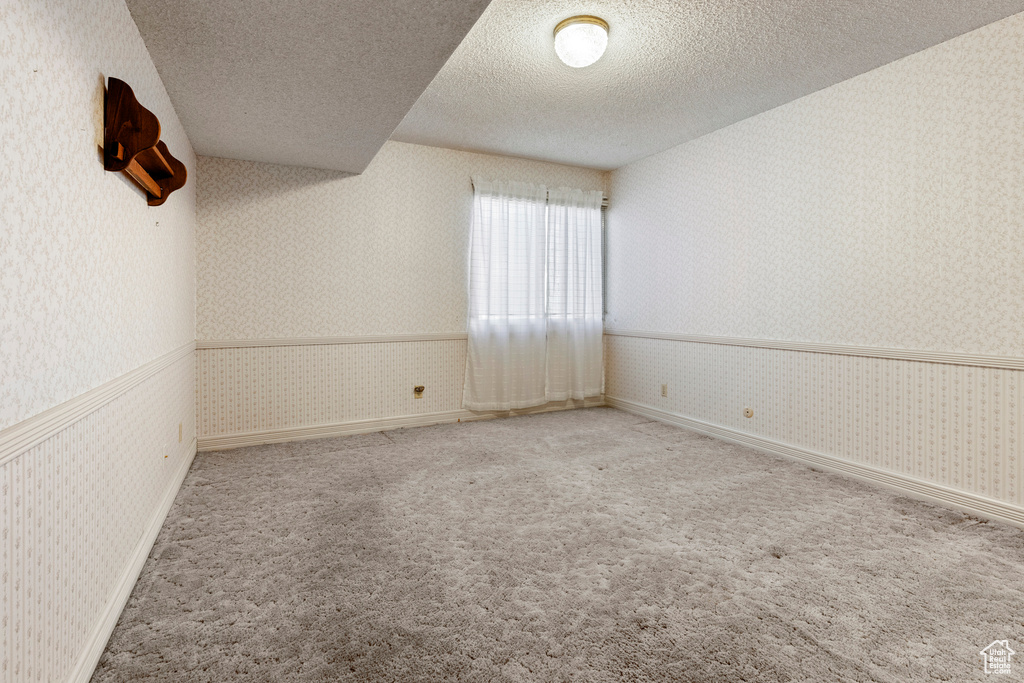 Carpeted empty room with a wainscoted wall, baseboards, wallpapered walls, and a textured ceiling