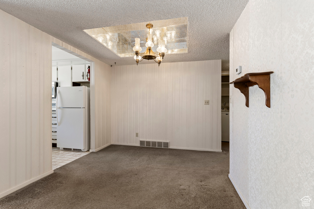 Unfurnished dining area with carpet flooring, a textured ceiling, visible vents, and an inviting chandelier