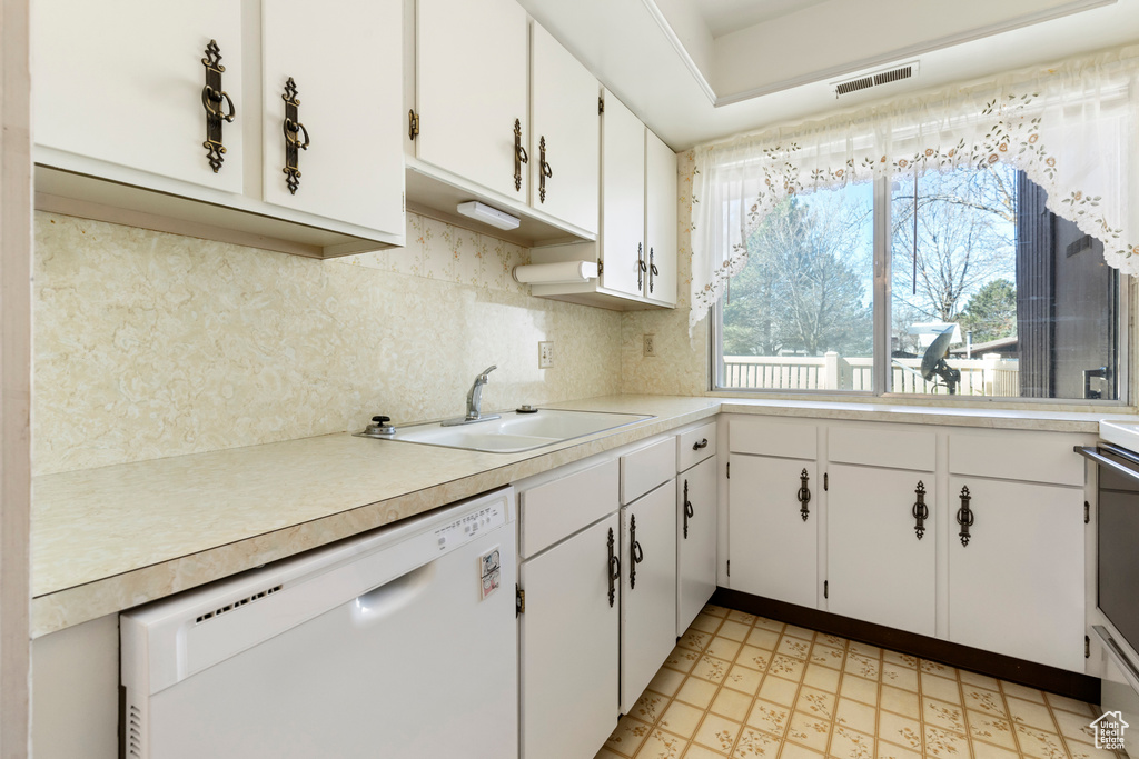 Kitchen featuring light countertops, light floors, a sink, white dishwasher, and backsplash