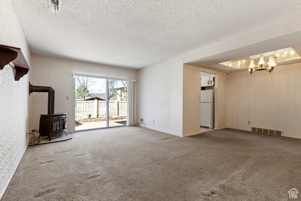Unfurnished living room featuring a wood stove, a chandelier, a textured ceiling, carpet floors, and visible vents