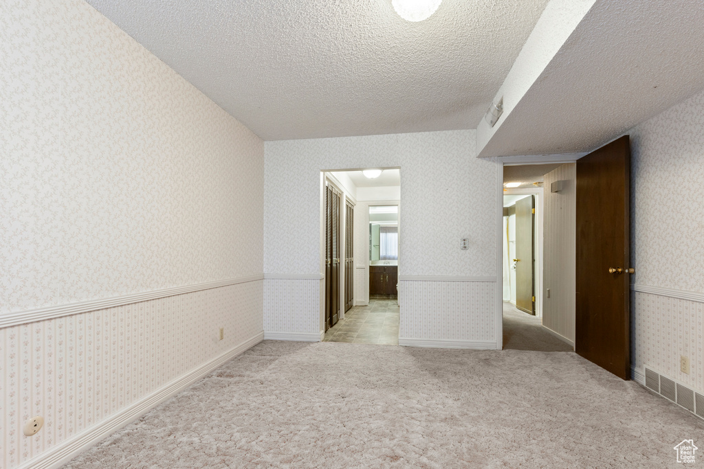 Unfurnished room featuring carpet flooring, a textured ceiling, visible vents, wallpapered walls, and wainscoting