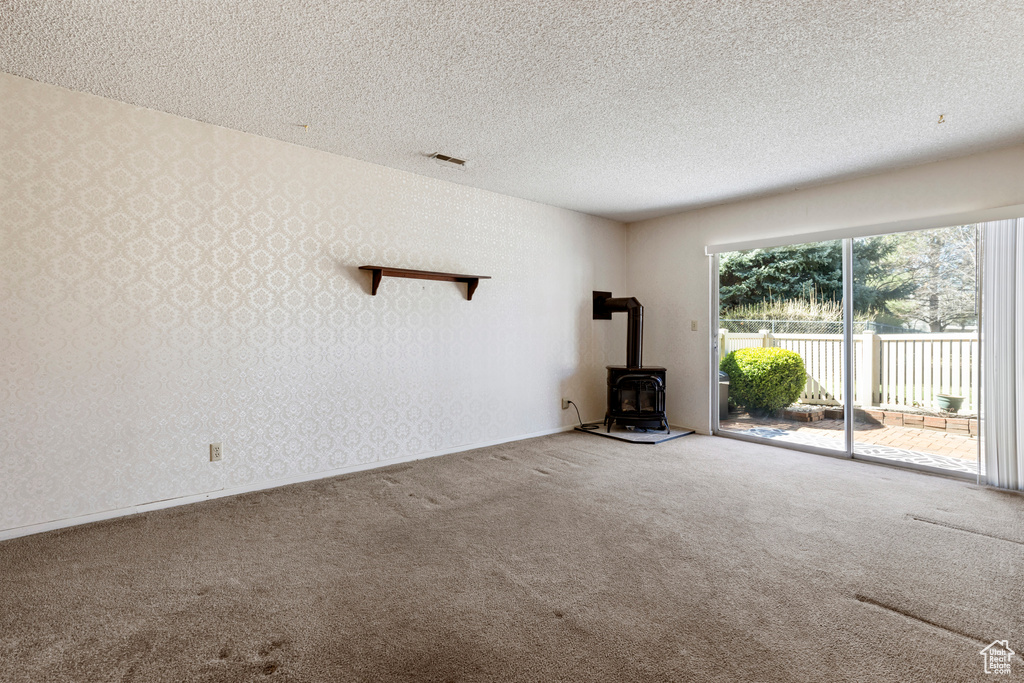 Unfurnished living room with carpet floors, a wood stove, a textured ceiling, visible vents, and wallpapered walls