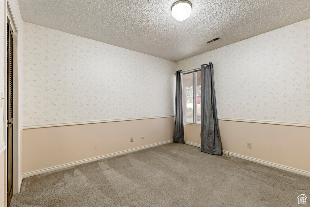 Unfurnished room featuring carpet, a textured ceiling, wallpapered walls, a wainscoted wall, and visible vents