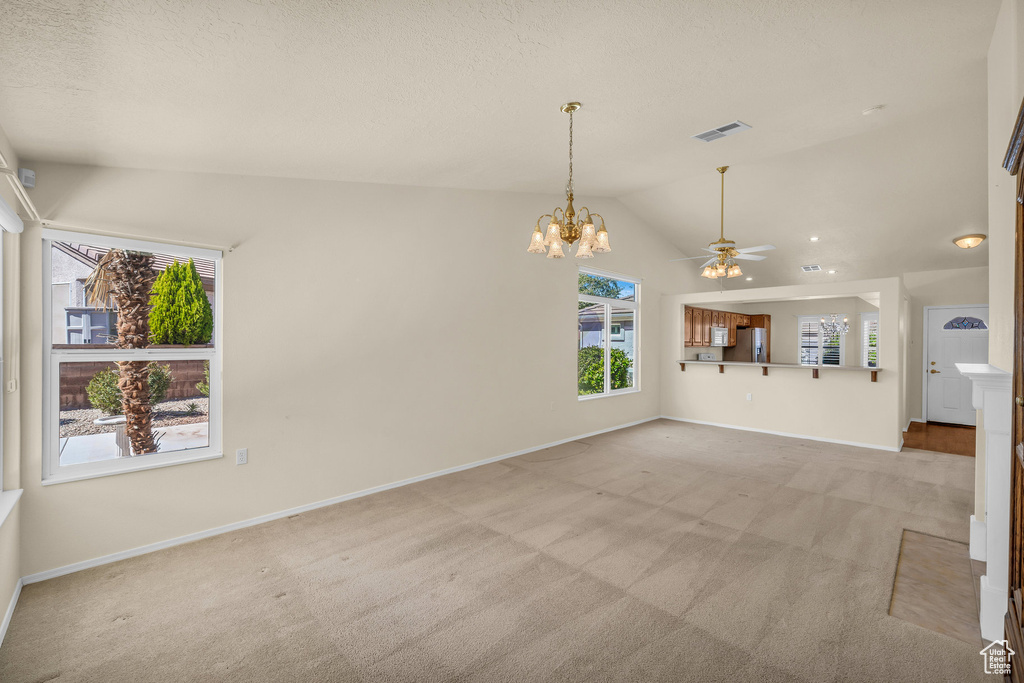 Unfurnished living room with lofted ceiling, light colored carpet, ceiling fan, a chandelier, and a textured ceiling