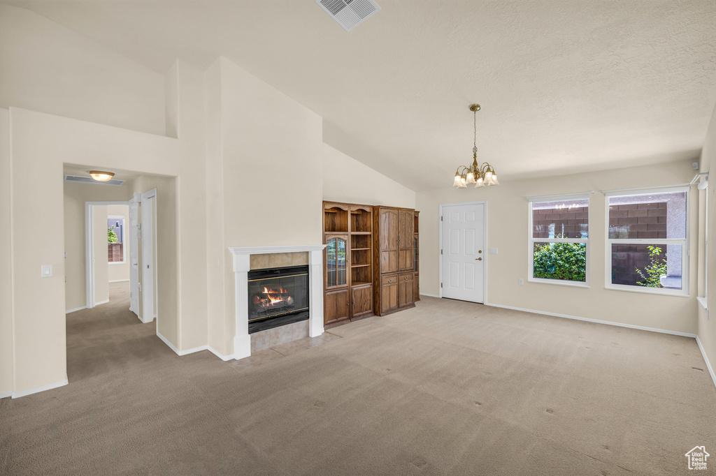 Unfurnished living room with light carpet, plenty of natural light, a tile fireplace, a chandelier, and high vaulted ceiling