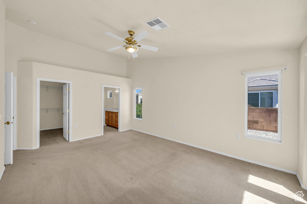 Unfurnished bedroom featuring light carpet, a spacious closet, a closet, ensuite bathroom, and lofted ceiling