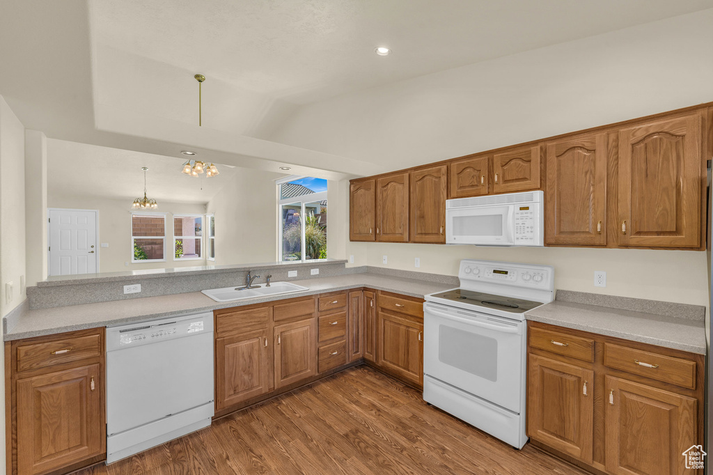 Kitchen with white appliances, a chandelier, vaulted ceiling, brown cabinets, and wood finished floors