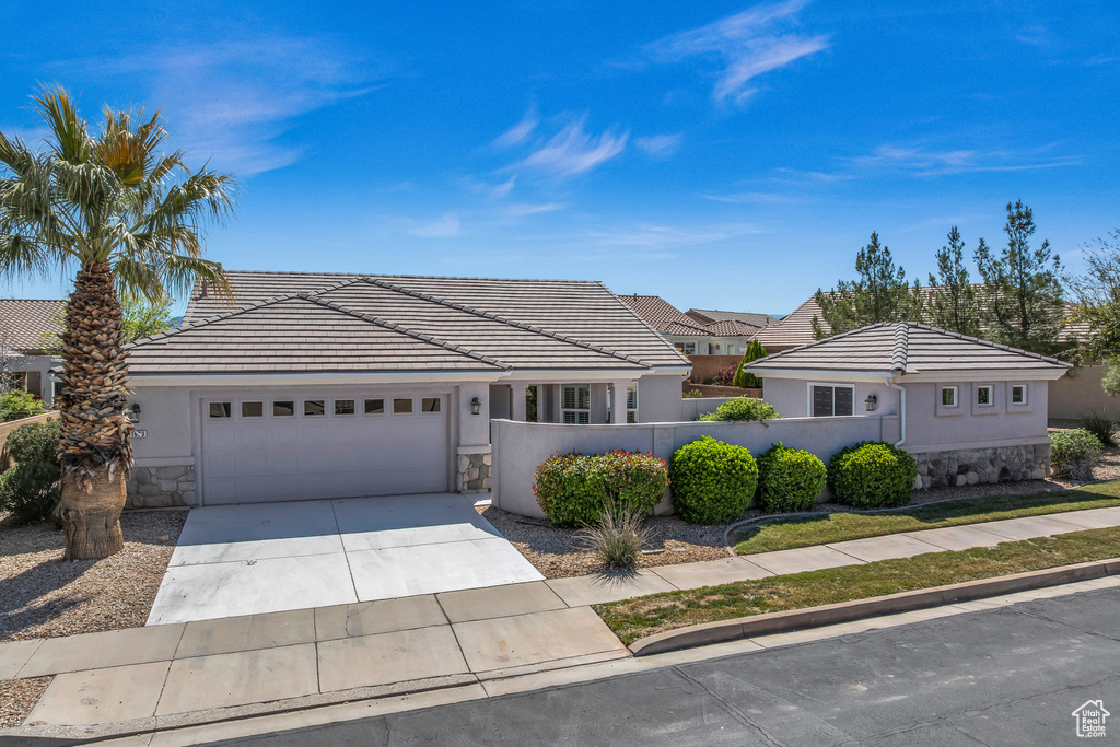 View of front facade featuring stone siding, an attached garage, a fenced front yard, driveway, and a tile roof