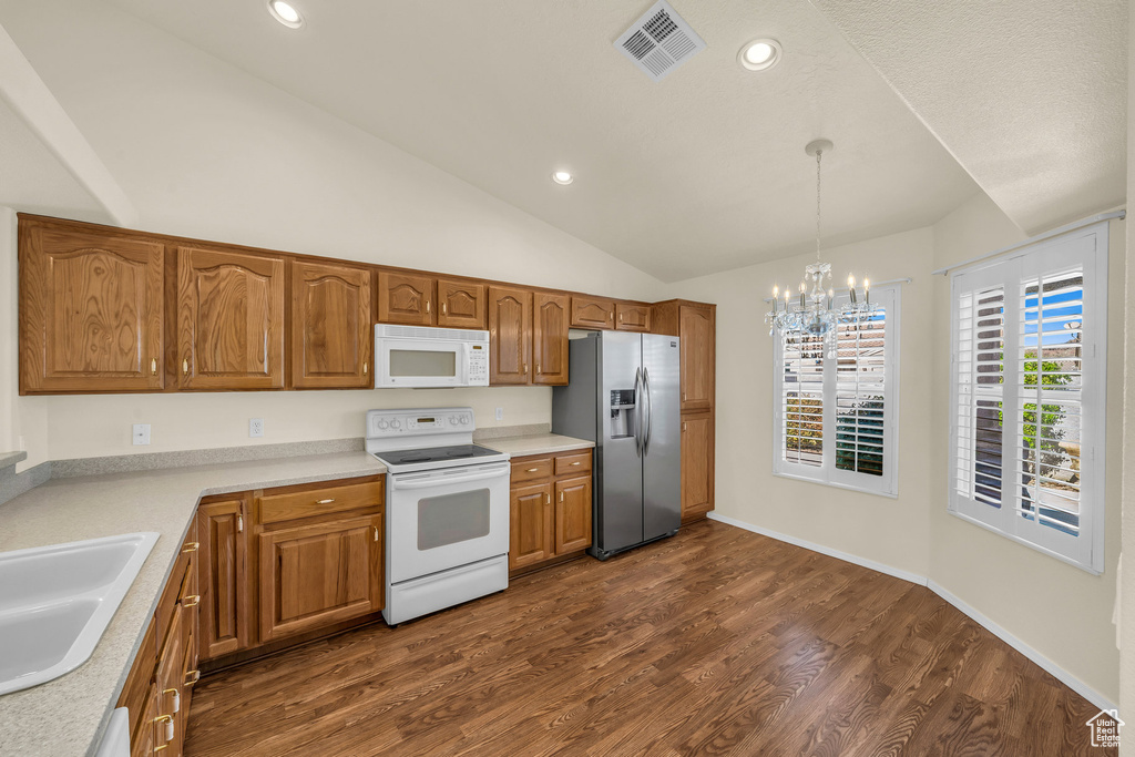 Kitchen with white appliances, a chandelier, dark wood-type flooring, light countertops, and lofted ceiling