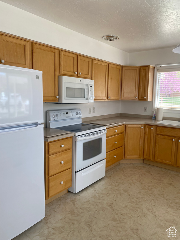 Kitchen with a textured ceiling, brown cabinets, white appliances, and a sink