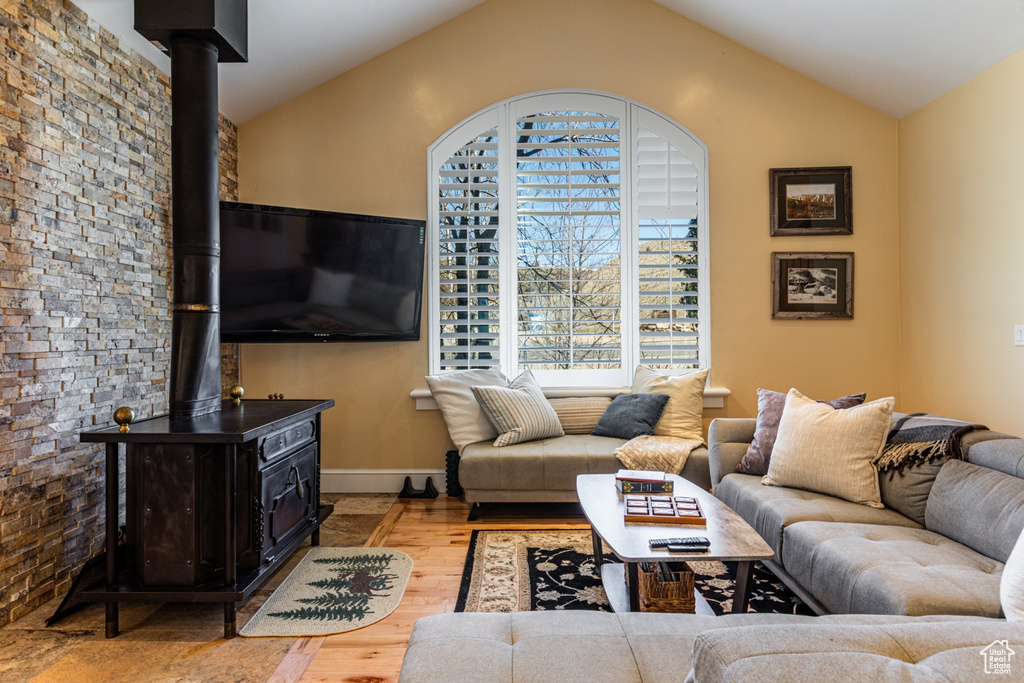 Living room with a wood stove, wood finished floors, and vaulted ceiling