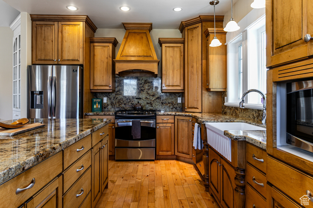 Kitchen featuring stainless steel appliances, custom range hood, brown cabinets, pendant lighting, and recessed lighting