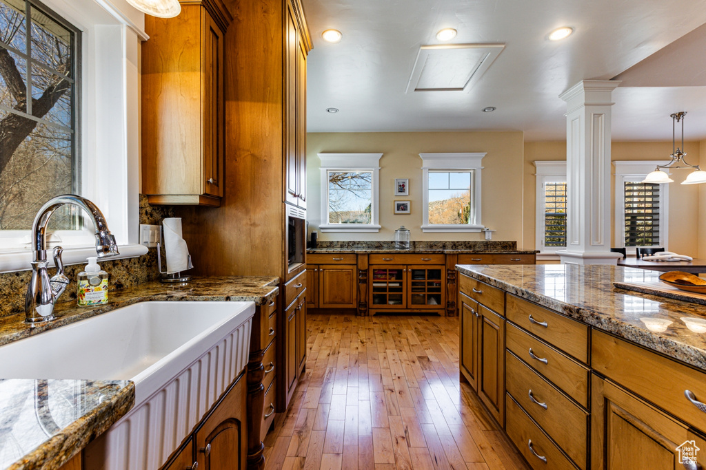 Kitchen with decorative columns, brown cabinetry, light wood finished floors, stone countertops, and recessed lighting