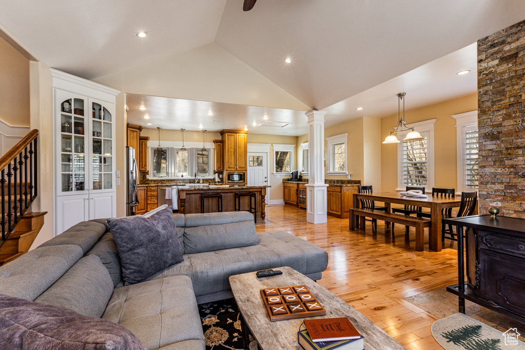Living room with ornate columns, light wood finished floors, vaulted ceiling, stairs, and recessed lighting