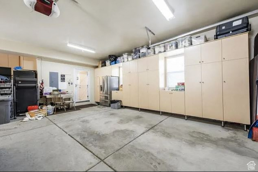 Garage with stainless steel refrigerator with ice dispenser, a garage door opener, and electric panel