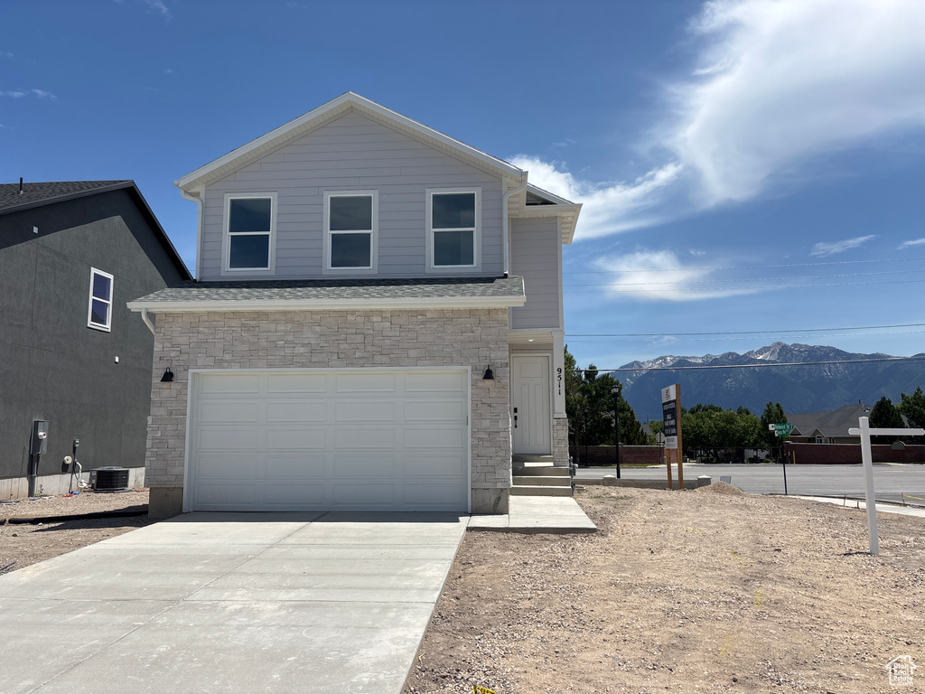 View of front of house with stone siding, a mountain view, concrete driveway, and a garage