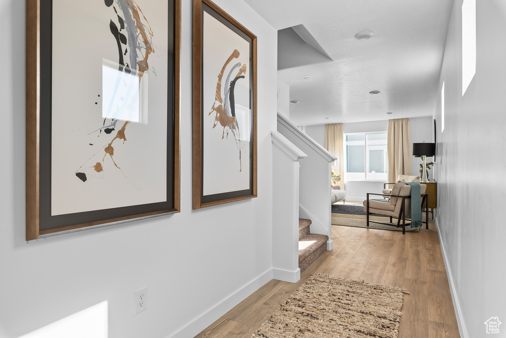 Hallway with light wood finished floors, stairs, and baseboards