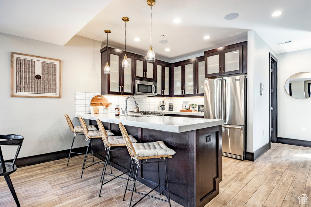 Kitchen with backsplash, light wood-style floors, a kitchen bar, appliances with stainless steel finishes, and a sink