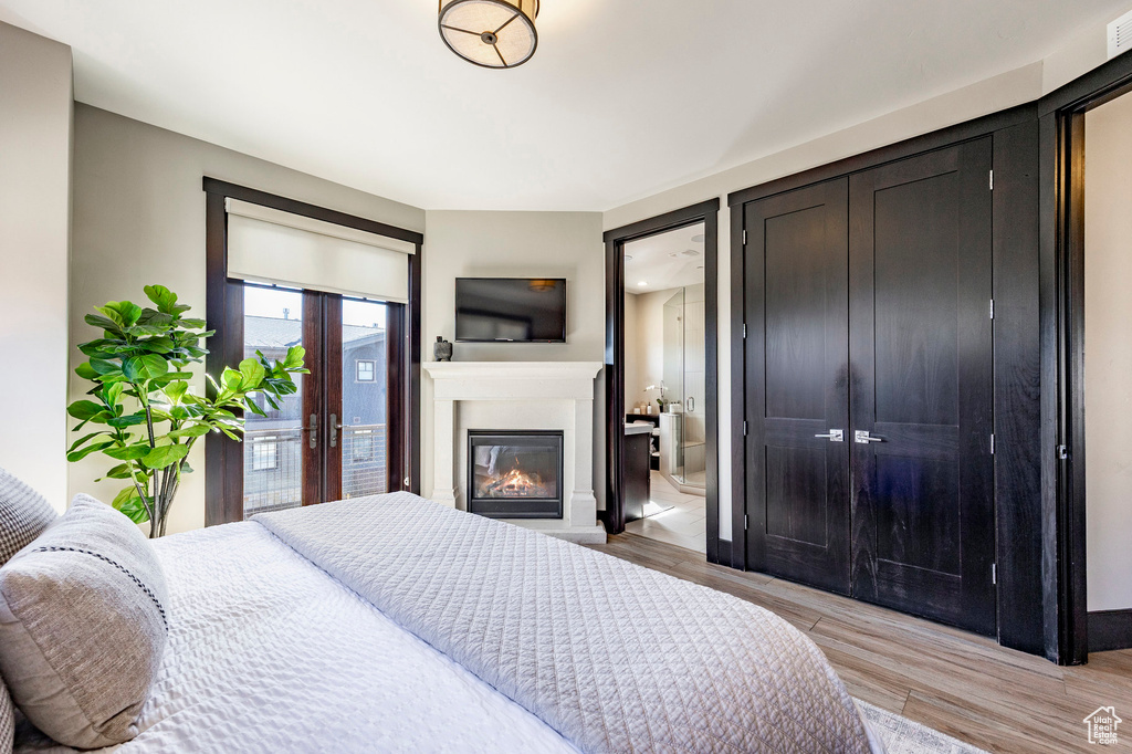 Bedroom featuring a glass covered fireplace, access to outside, baseboards, connected bathroom, and light wood-style floors