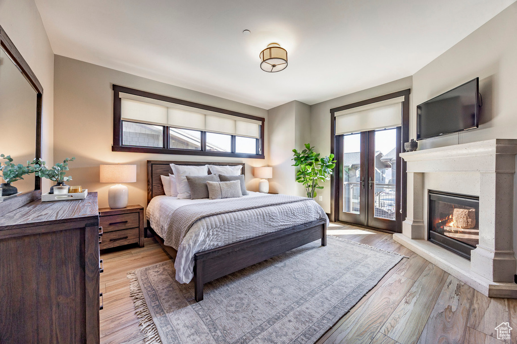 Bedroom with a glass covered fireplace, light wood-style floors, and access to exterior
