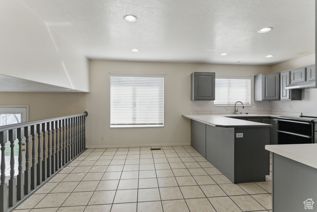 Kitchen featuring light countertops, gray cabinets, a sink, light tile patterned flooring, and a peninsula