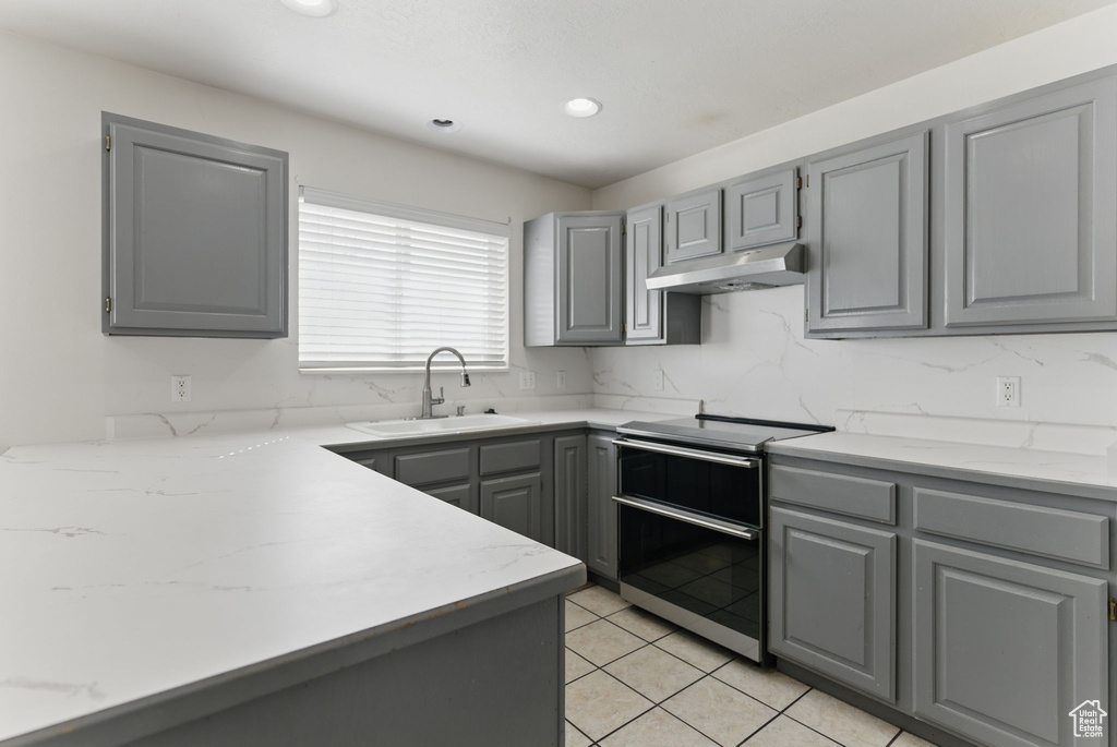 Kitchen featuring under cabinet range hood, gray cabinetry, a sink, light tile patterned flooring, and range with two ovens