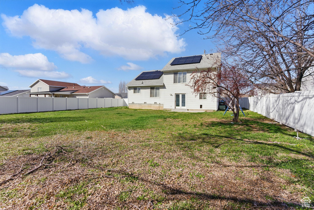 Rear view of property featuring roof mounted solar panels, a patio, a fenced backyard, roof with shingles, and a yard