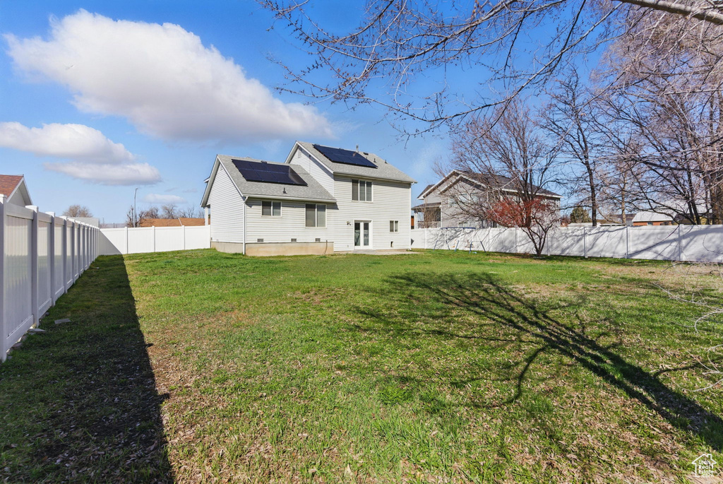 Rear view of house featuring a lawn, a fenced backyard, and roof mounted solar panels