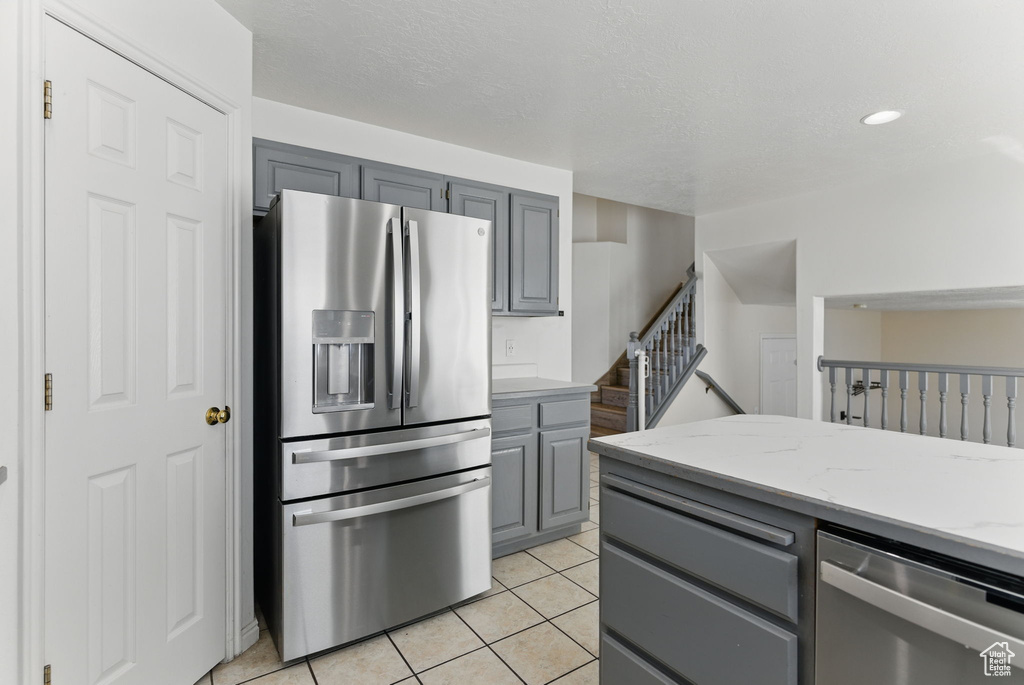 Kitchen featuring light tile patterned flooring, light stone countertops, stainless steel appliances, recessed lighting, and gray cabinets