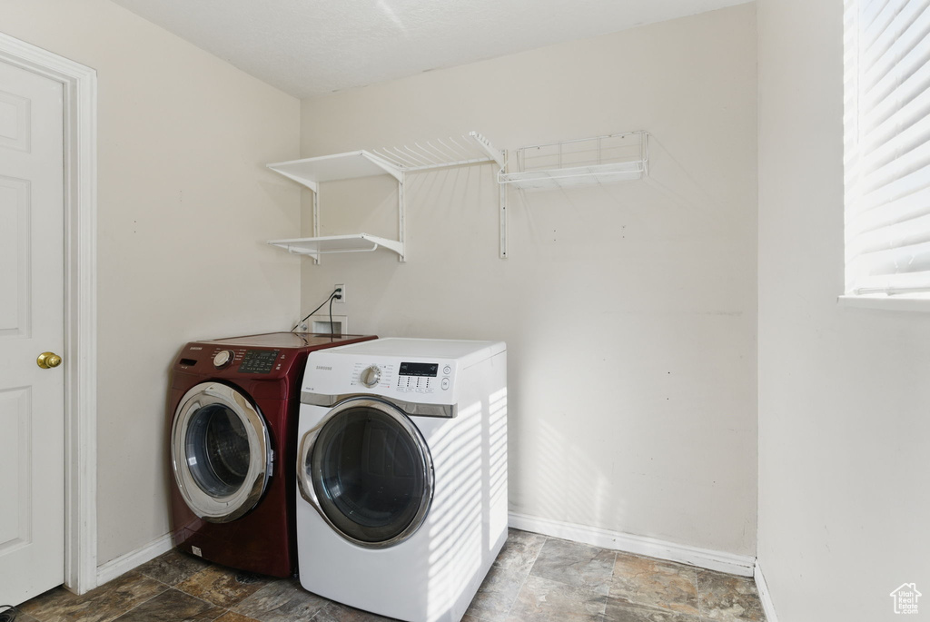 Washroom featuring washing machine and clothes dryer, baseboards, laundry area, and stone finish flooring