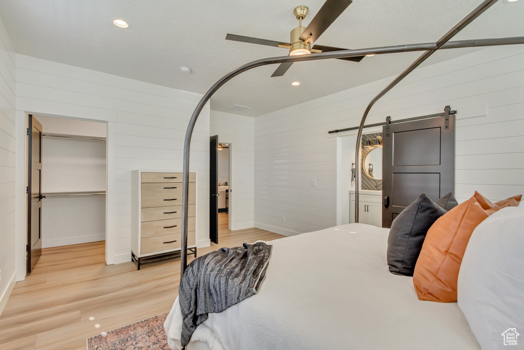 Bedroom with a barn door, wood finished floors, wood walls, ceiling fan, and recessed lighting