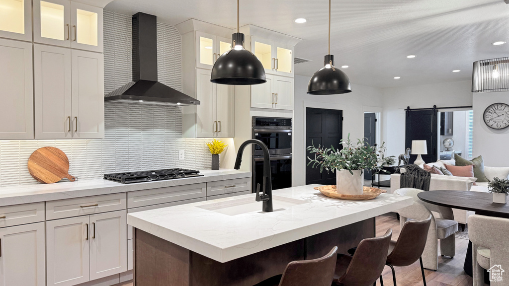 Kitchen featuring a sink, double oven, wall chimney exhaust hood, white cabinetry, and stainless steel gas stovetop