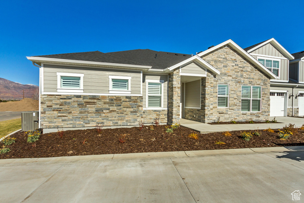 View of front of property featuring stone siding, driveway, central AC unit, and an attached garage