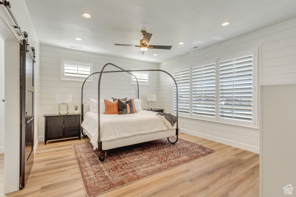 Bedroom featuring a textured ceiling, visible vents, light wood finished floors, recessed lighting, and a barn door