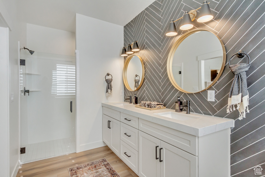 Full bath with wood finished floors, a sink, double vanity, and a walk in shower