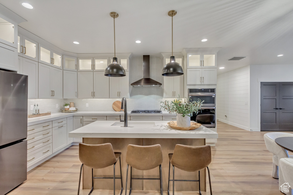 Kitchen with light countertops, stainless steel appliances, light wood finished floors, visible vents, and wall chimney range hood