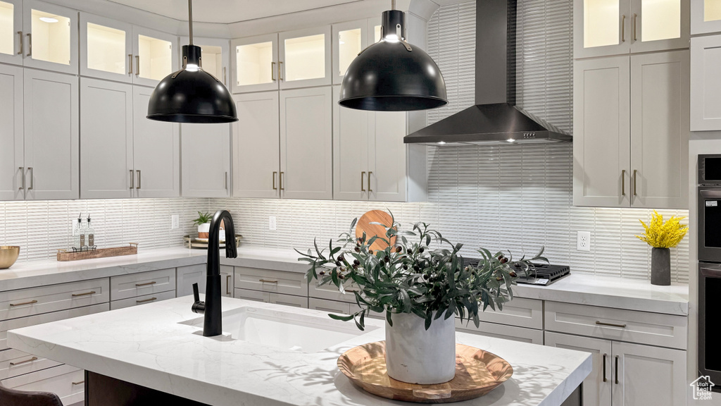 Kitchen featuring a sink, wall chimney exhaust hood, light stone counters, and tasteful backsplash