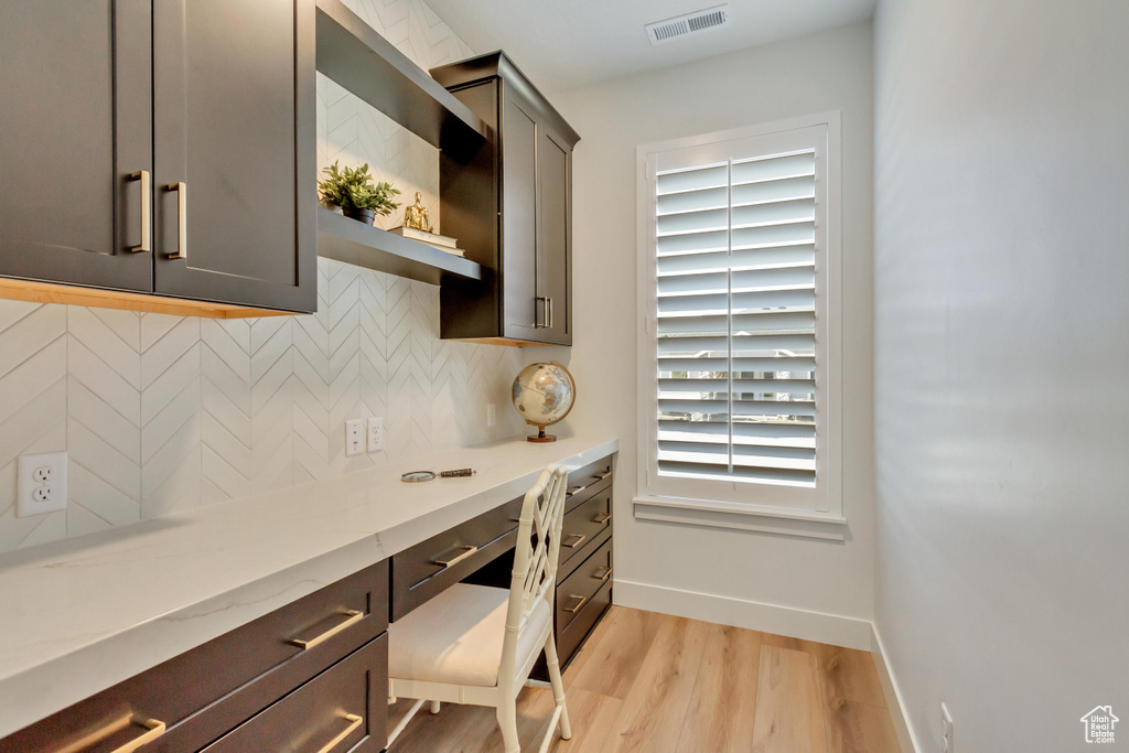Kitchen with built in desk, light wood-type flooring, baseboards, backsplash, and visible vents