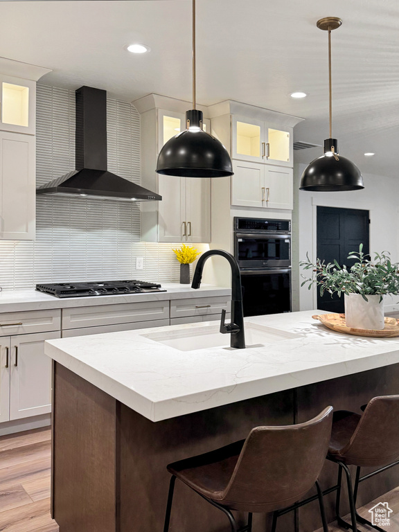 Kitchen featuring stainless steel gas cooktop, a sink, tasteful backsplash, wall chimney range hood, and multiple ovens
